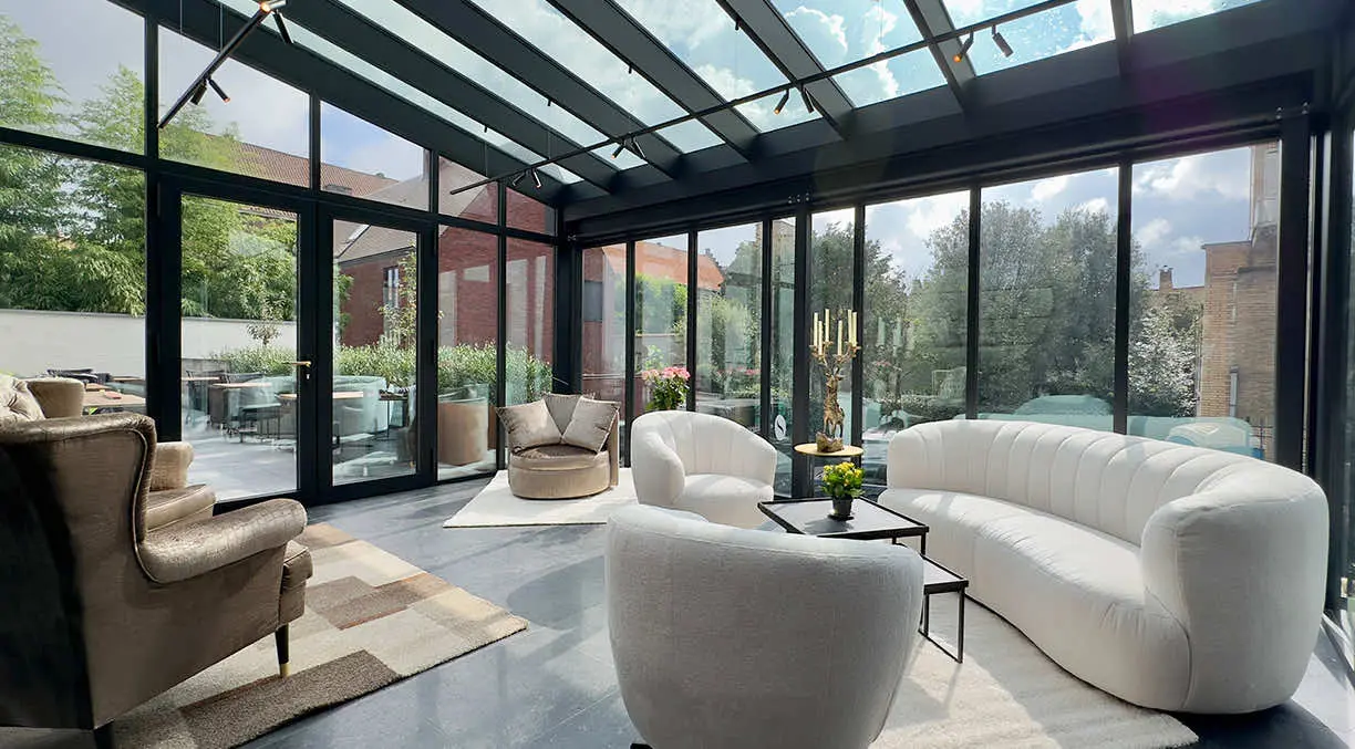 Wintertuin met glazen dak, witte designbanken en fauteuils, met zicht op de tuin